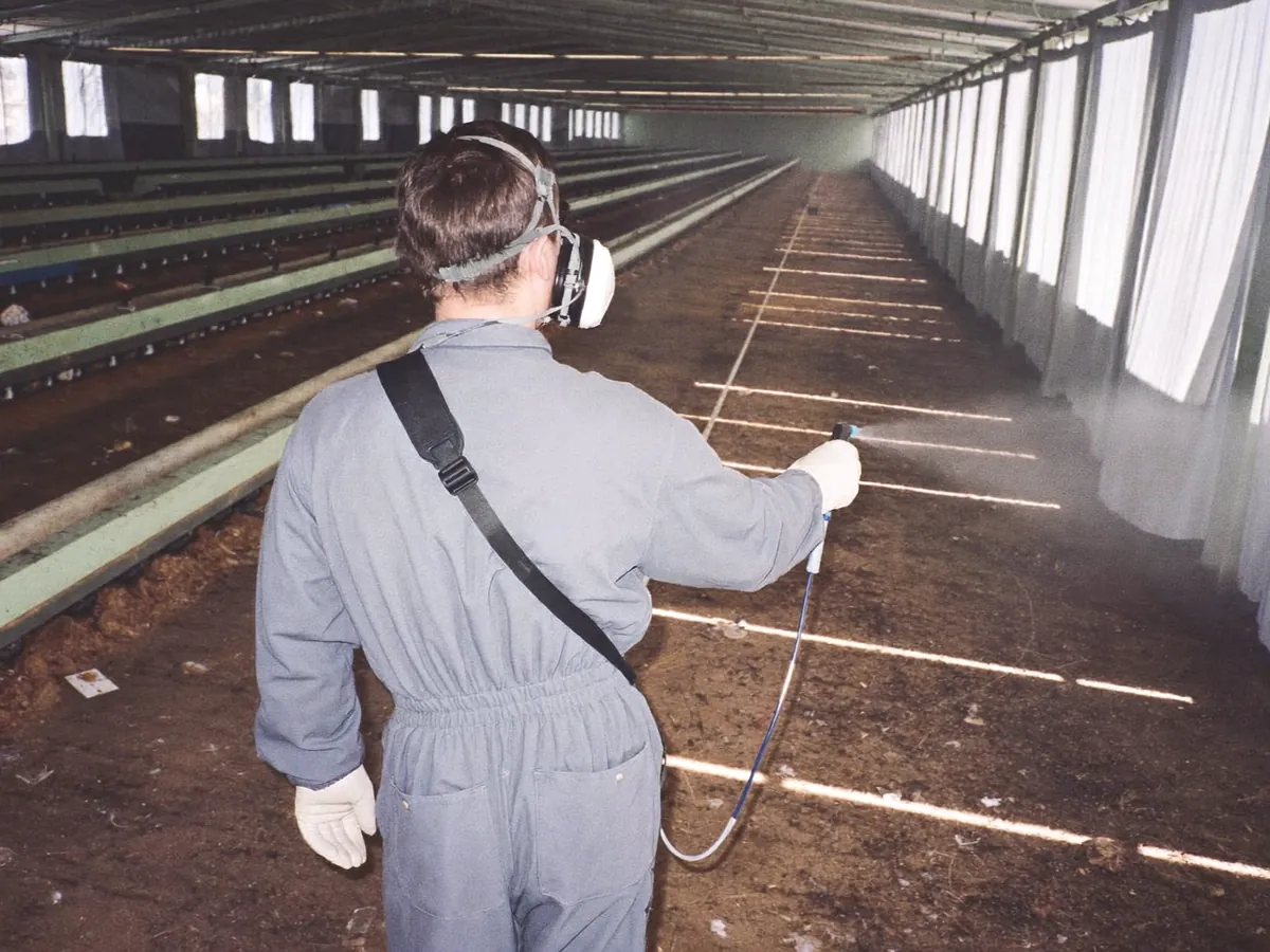 A technician in protective gear spraying an empty poultry house